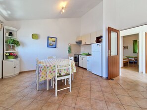 A compact kitchen with white cabinets, a dining table with a colorful tablecloth, and a small refrigerator.