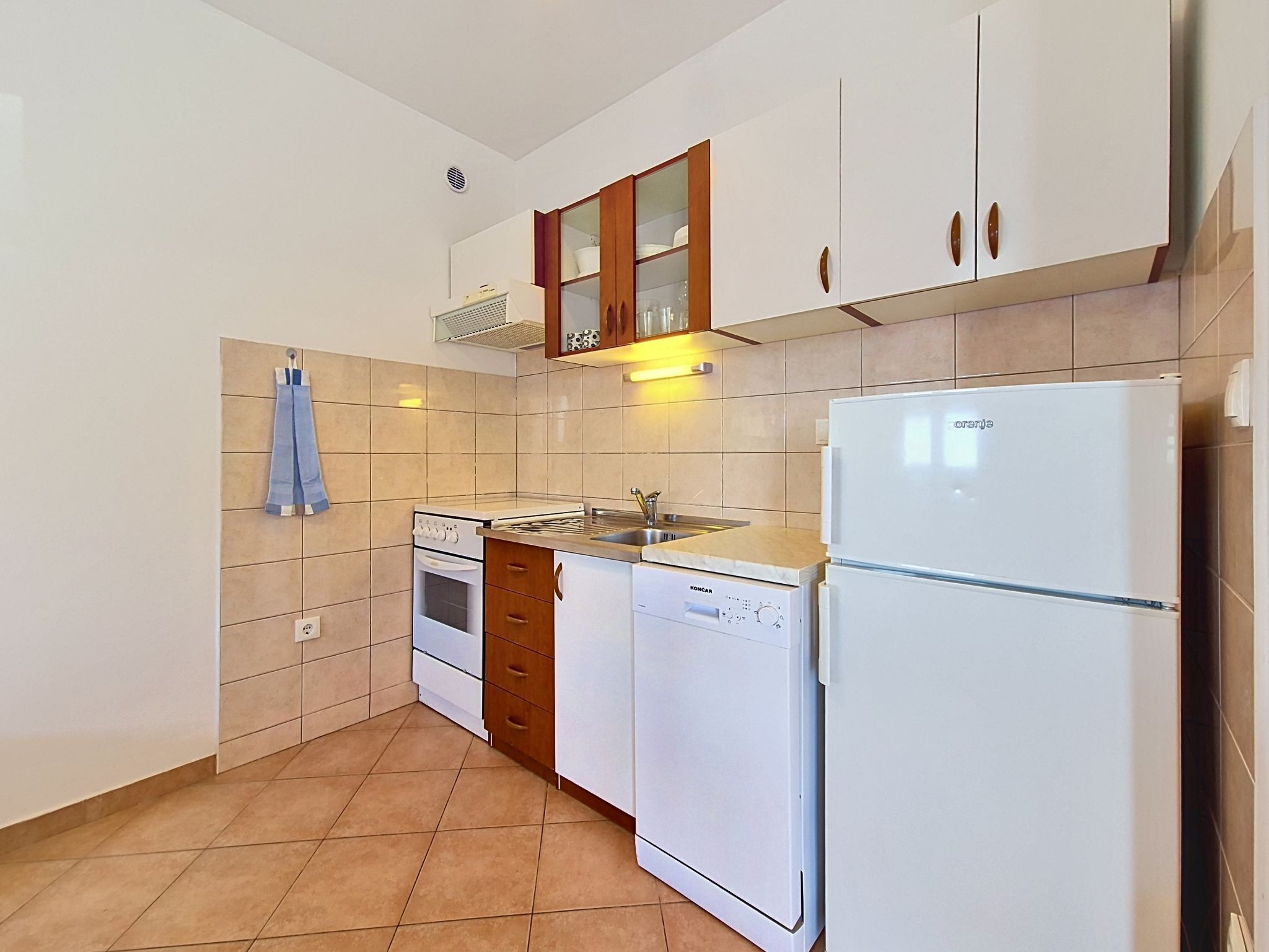 A kitchen with white appliances, wooden cabinets, and a tiled floor.