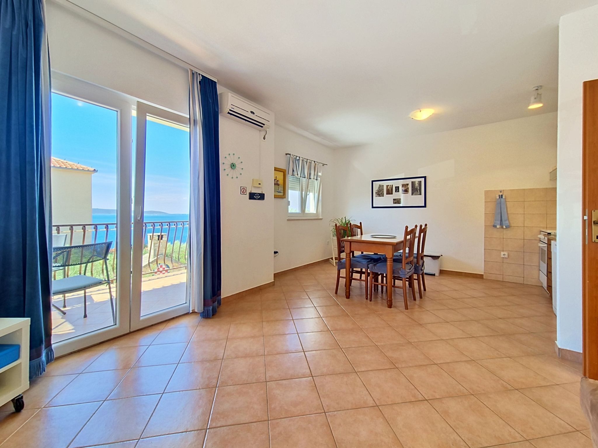 A room with a dining table, chairs, a view of the sea, and a balcony with a chair.