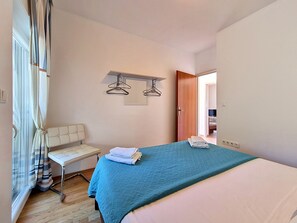 Une chambre à coucher comprenant un lit, une table de chevet, une chaise, une lampe suspendue et une porte donnant sur une autre pièce.