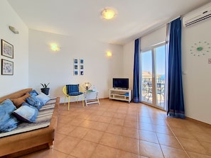 Un salon avec un canapé, un téléviseur, une petite table et une chaise.