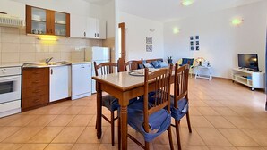 A modern kitchen with white cabinets, a dining table with chairs, a TV, and a sofa in a living area. - Apartment Culić by Interhome (Trogir)