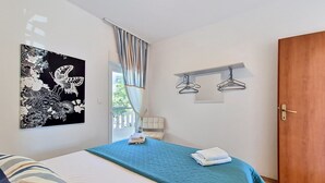 A bedroom with a bed, a wall-mounted artwork, a window with curtains, a door, and a coat rack. - Apartment Culić by Interhome (Trogir)