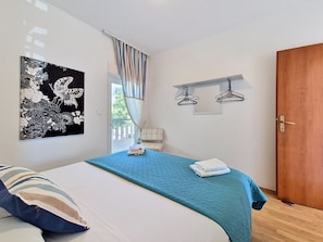 Une chambre à coucher comprenant un lit, une œuvre d’art accrochée au mur, une fenêtre avec des rideaux, une porte et un porte-manteau.