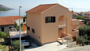 A two-story building with a red-tiled roof, a balcony, and a view of the sea.
