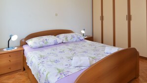 A bedroom with a wooden bed, a nightstand with a lamp, a wardrobe, and a wall-mounted light.