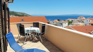 A balcony with a table and chairs, overlooking a coastal town with terracotta roofs.