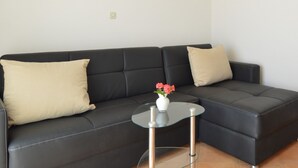A black leather sofa with two beige cushions, a glass coffee table with a vase of pink flowers, and a framed picture on the wall.