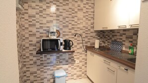 A compact kitchen with a microwave, coffee maker, and kettle on a shelf, a small trash bin, and a sink with a patterned backsplash. - Apartment Viktor by Interhome (Trogir)