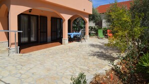 A two-story building with a stone patio, outdoor seating, and a view of a red-tiled roof building in the background. - Apartment Viktor by Interhome (Trogir)