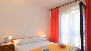 A neatly made bed with white and yellow bedding, two bedside lamps, and a window with red curtains. - Apartment Viktor by Interhome (Trogir)