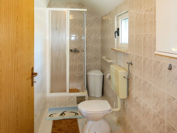 A bathroom with a shower, toilet, and a small window.