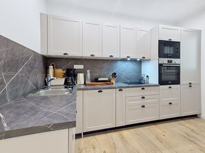 A modern kitchen with white cabinets, a marble backsplash, and a built-in oven.