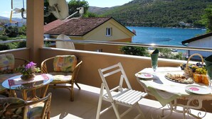 A balcony with a table set for dining, chairs, and a view of the sea and hills. - Apartment Perisa by Interhome (Šibenik)