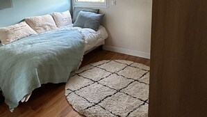 A bedroom with a bed, a window with blinds, a ceiling light, and a round rug. - Les Pieds Dans L'eau ! Accès Direct sur la Plage de Bonne Source (Pornichet)