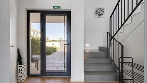A modern interior with a glass door leading outside, a staircase with a metal railing, and a wall-mounted light fixture. - Vacation home Carmen by Interhome (Zaton (Šibenik))