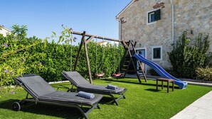 A backyard with a stone building, a swing set, a slide, and two sun loungers. - Vacation home Carmen by Interhome (Zaton (Šibenik))
