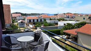 A balcony with a table and chairs, overlooking a coastal town with red-tiled roofs and a clear sky. - Apartment Josip by Interhome (Vodice)