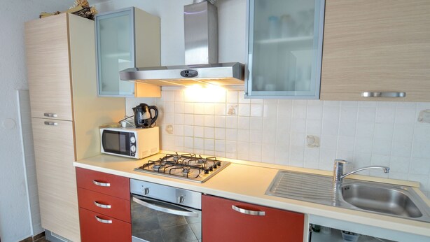 A compact kitchen with a gas stove, microwave, oven, and stainless steel sink.