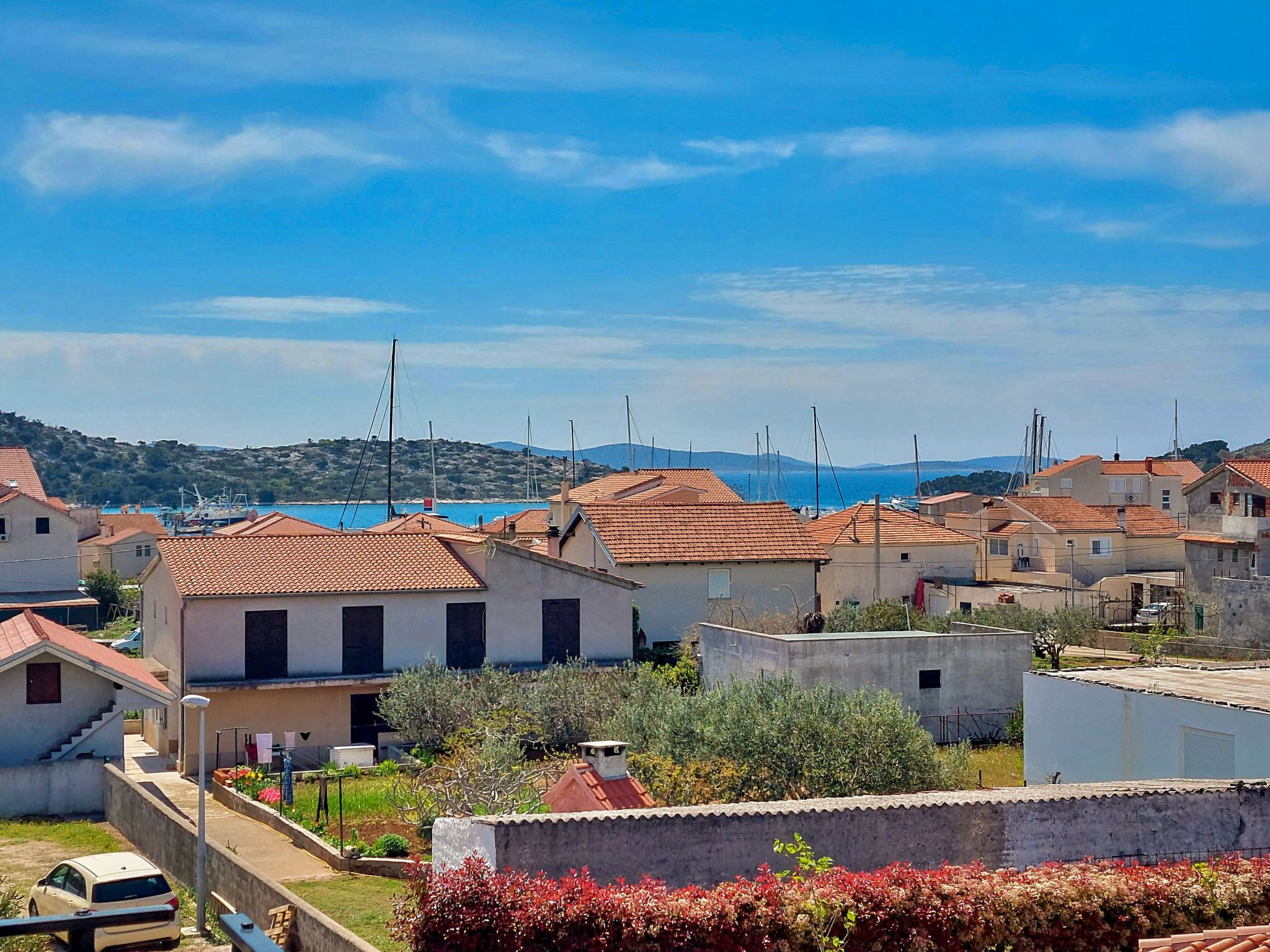 Una zona residencial costera con casas de techo de teja terracota, un cielo azul despejado y vista al mar.