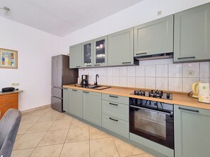 A kitchen with light green cabinets, a stainless steel refrigerator, a gas stove, and a tiled backsplash.