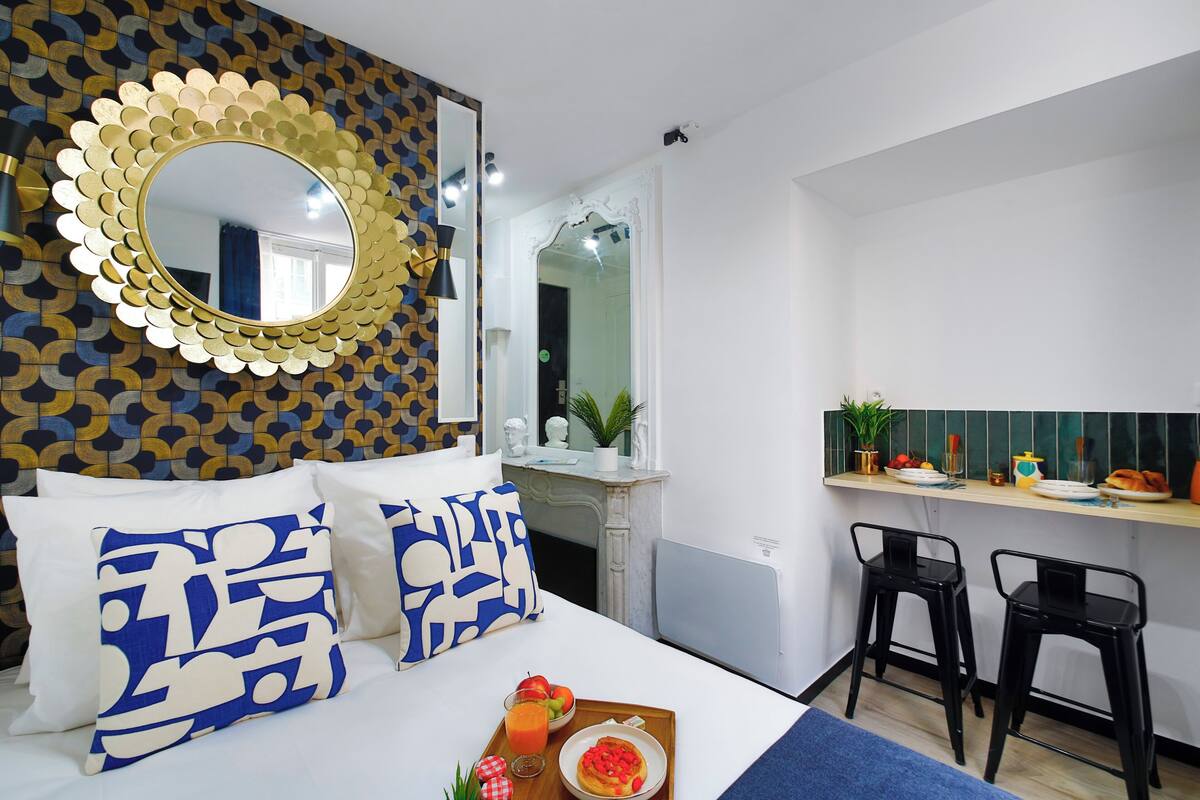 A hotel room with a bed, a breakfast bar, and a mirror with a decorative frame.