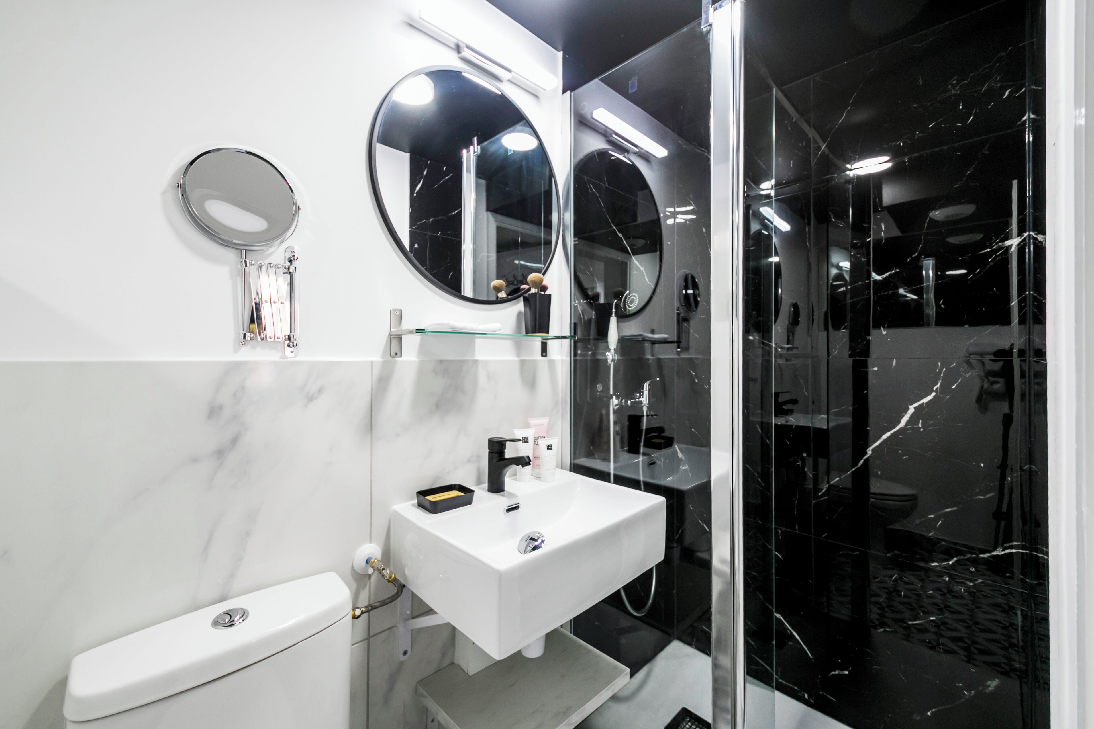 Un baño moderno con un lavamanos blanco, dos espejos redondos y una cabina de ducha de vidrio.