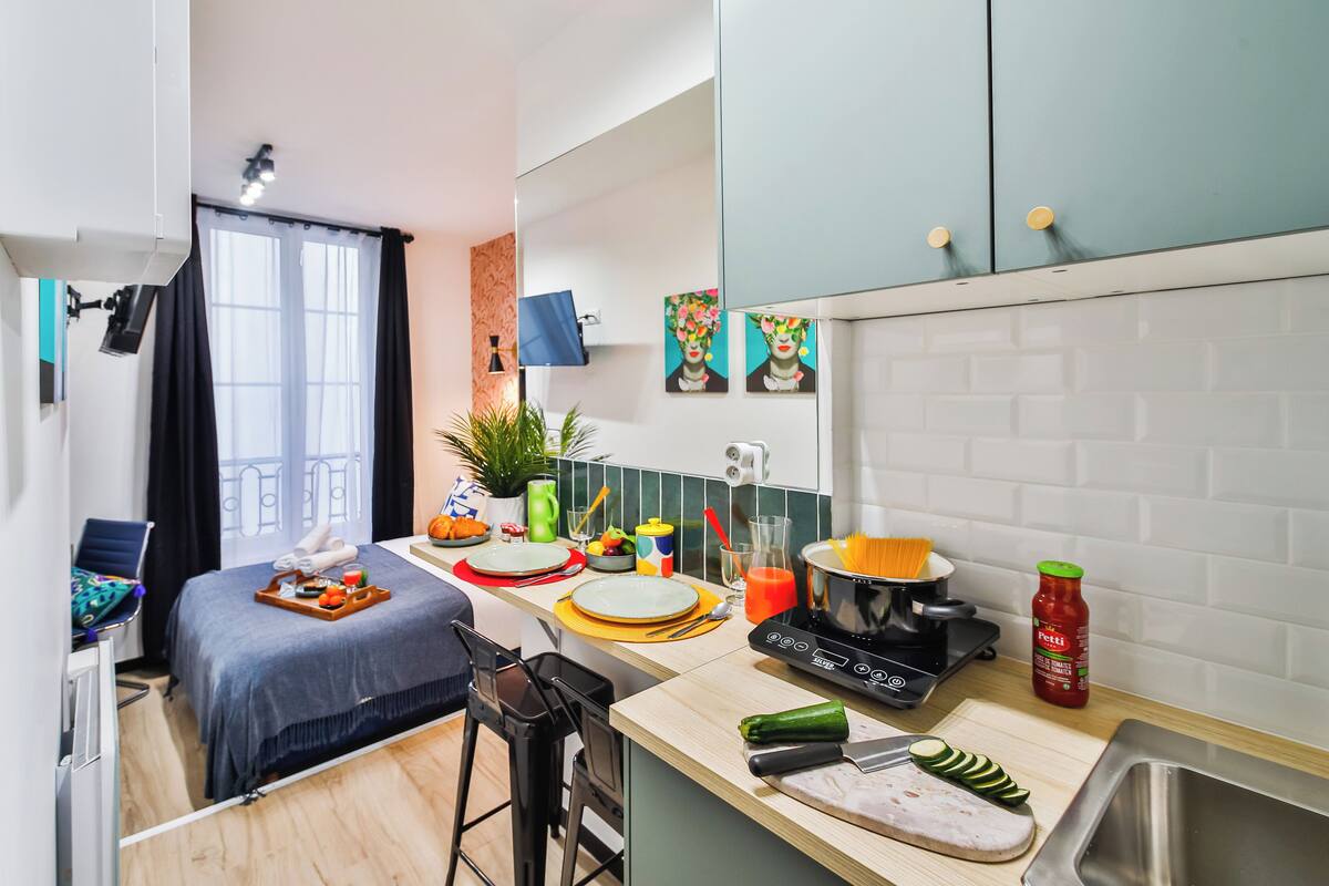 A compact hotel room with a bed, a small kitchenette, a dining area, and a bathroom.
