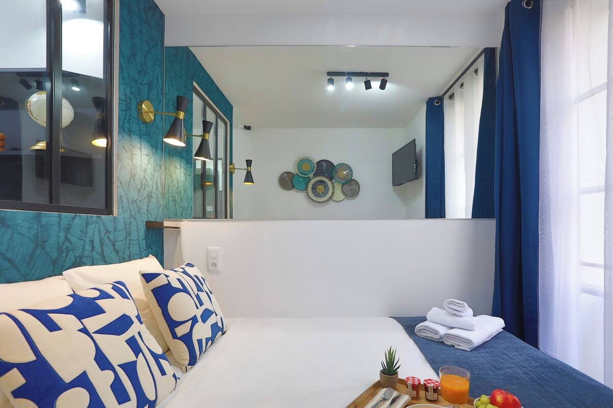 A hotel room with a bed, a small table with breakfast items, a potted plant, and a wall-mounted TV.