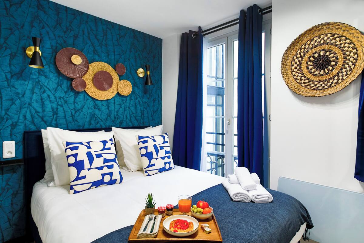 A hotel room with a bed, a tray with breakfast, a window with curtains, and a wall with decorative items.