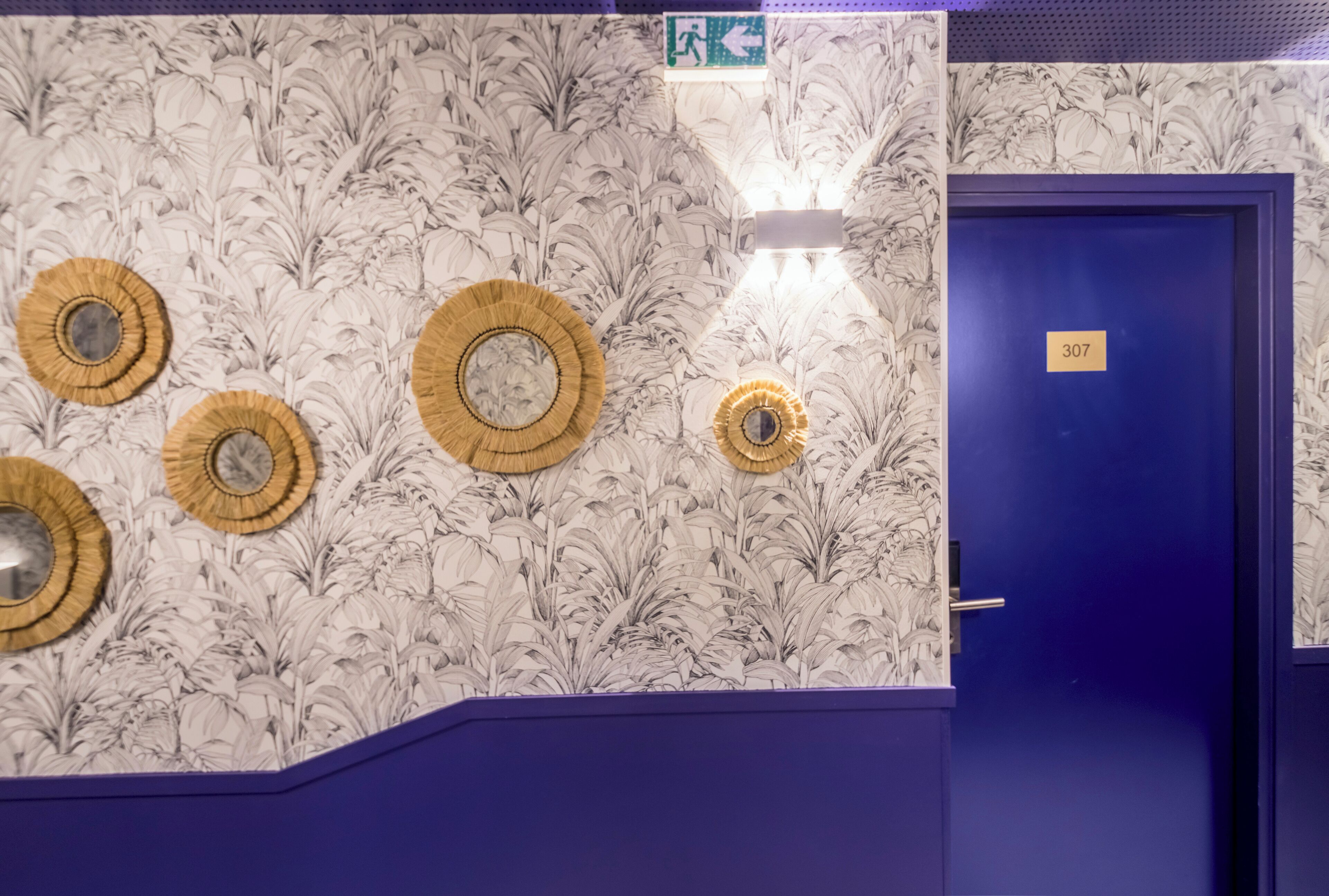 Una habitación con puerta azul identificada con el número 307, papel tapiz floral y cuatro adornos circulares en la pared.