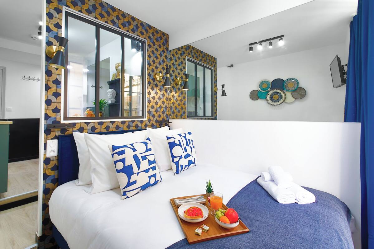 A modern hotel room with a large bed, a tray with breakfast, and decorative wall art.