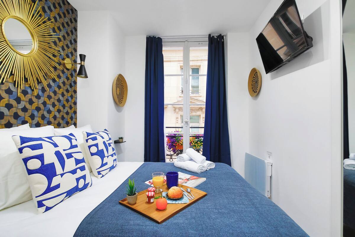A hotel room with a bed, a tray with breakfast items, a TV, and a window with curtains.