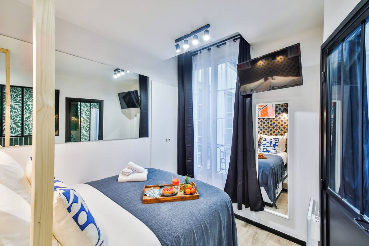 A modern hotel room with a bed, a tray with breakfast, a TV, and a balcony with a view.