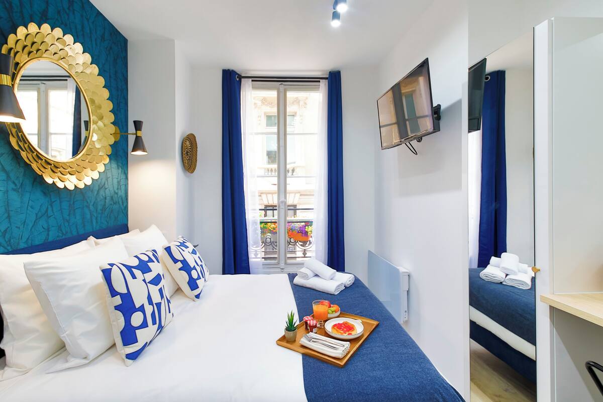 A hotel room with a bed, a breakfast tray, a TV, and a view of the outside balcony.