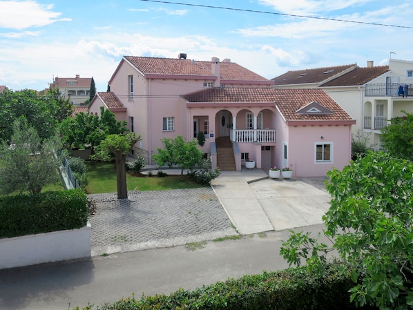 A pink villa with a tiled roof, a central staircase, and a small balcony.