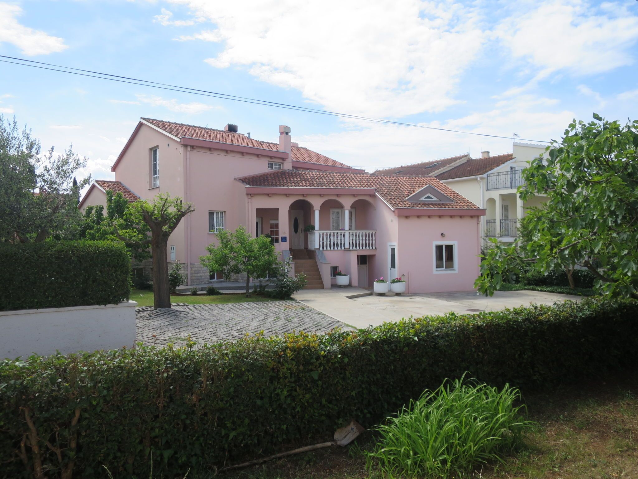 A pink villa with a tiled roof, a balcony, and a well-maintained garden.