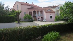 A pink villa with a tiled roof, a balcony, and a well-maintained garden.