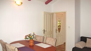 A dining area with a wooden table, four chairs, a vase with flowers, and a door in the background.