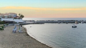 A beach with a row of sun loungers and a building with a balcony overlooking the sea.