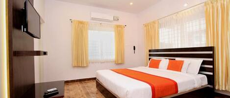 A bedroom with a bed, a desk, a television, and an air conditioning unit.