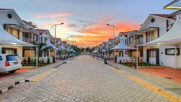 A row of modern, white houses with red roofs, arranged along a paved street with yellow tactile paving.