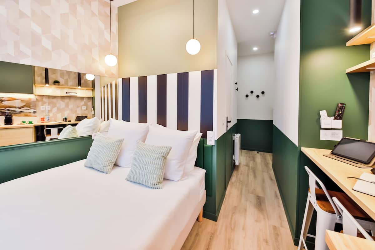 A modern hotel room with a large bed, a desk with a laptop, and a small kitchenette area.