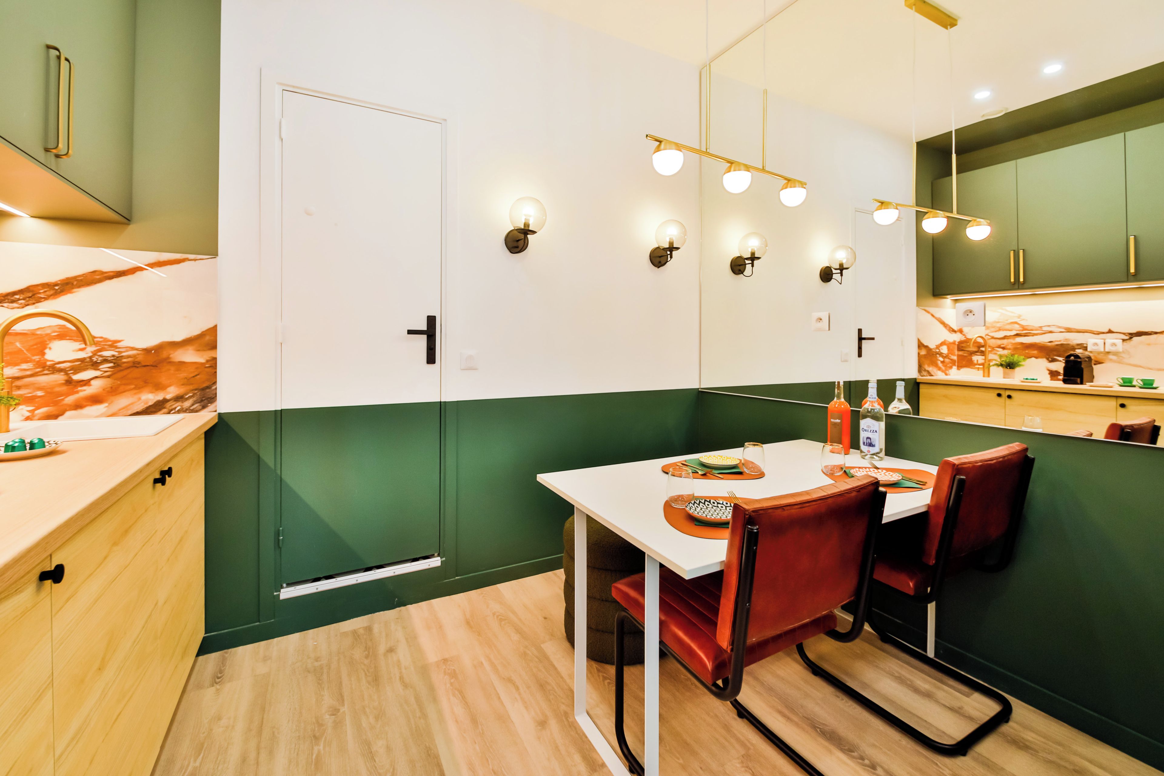 Une cuisine moderne avec des meubles de rangement verts et blancs, un pare-feu en marbre et un coin repas comprenant une table blanche et des chaises rouges.