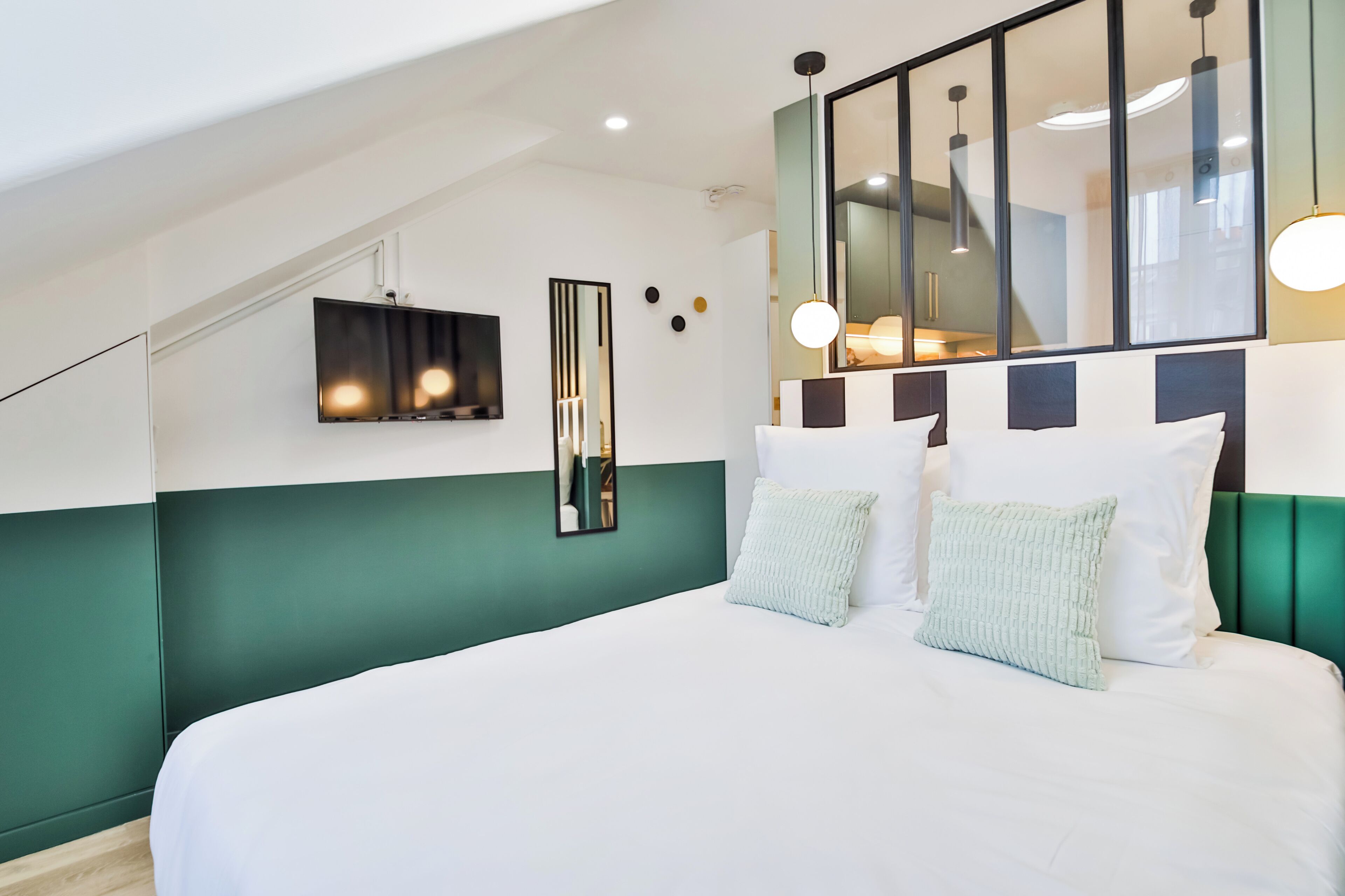 A modern bedroom with a large bed, a TV mounted on the wall, and a large mirror reflecting the room.