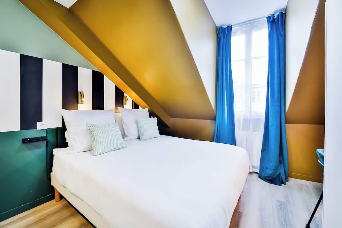 A modern bedroom with a large bed, a green accent wall, and a window with blue curtains.