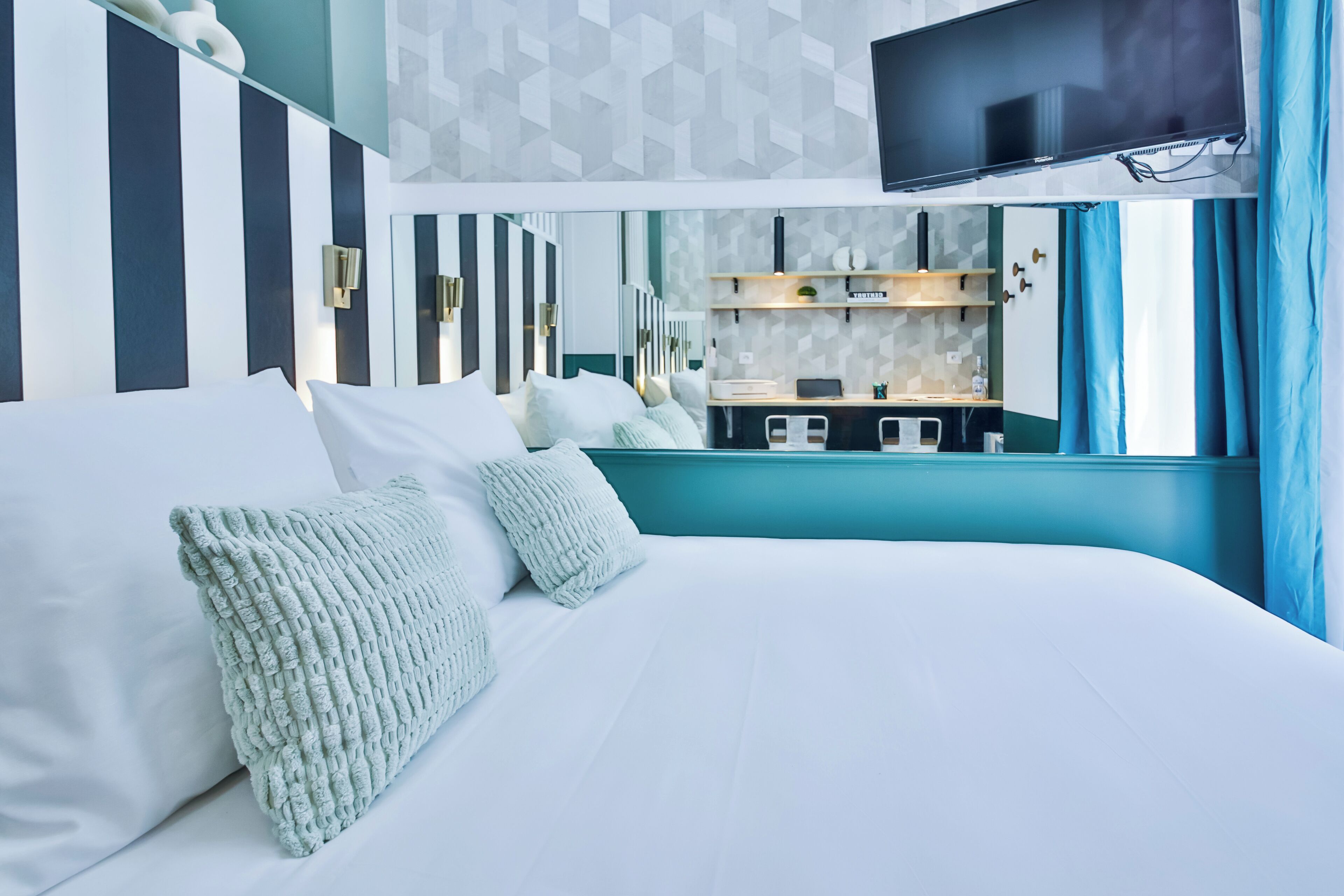 A modern hotel room with a large bed, a TV mounted on the wall, and a view of the kitchen area.