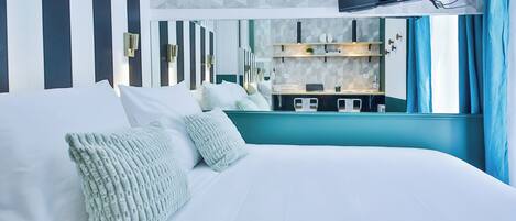 A modern hotel room with a large bed, a TV mounted on the wall, and a view of the kitchen area.