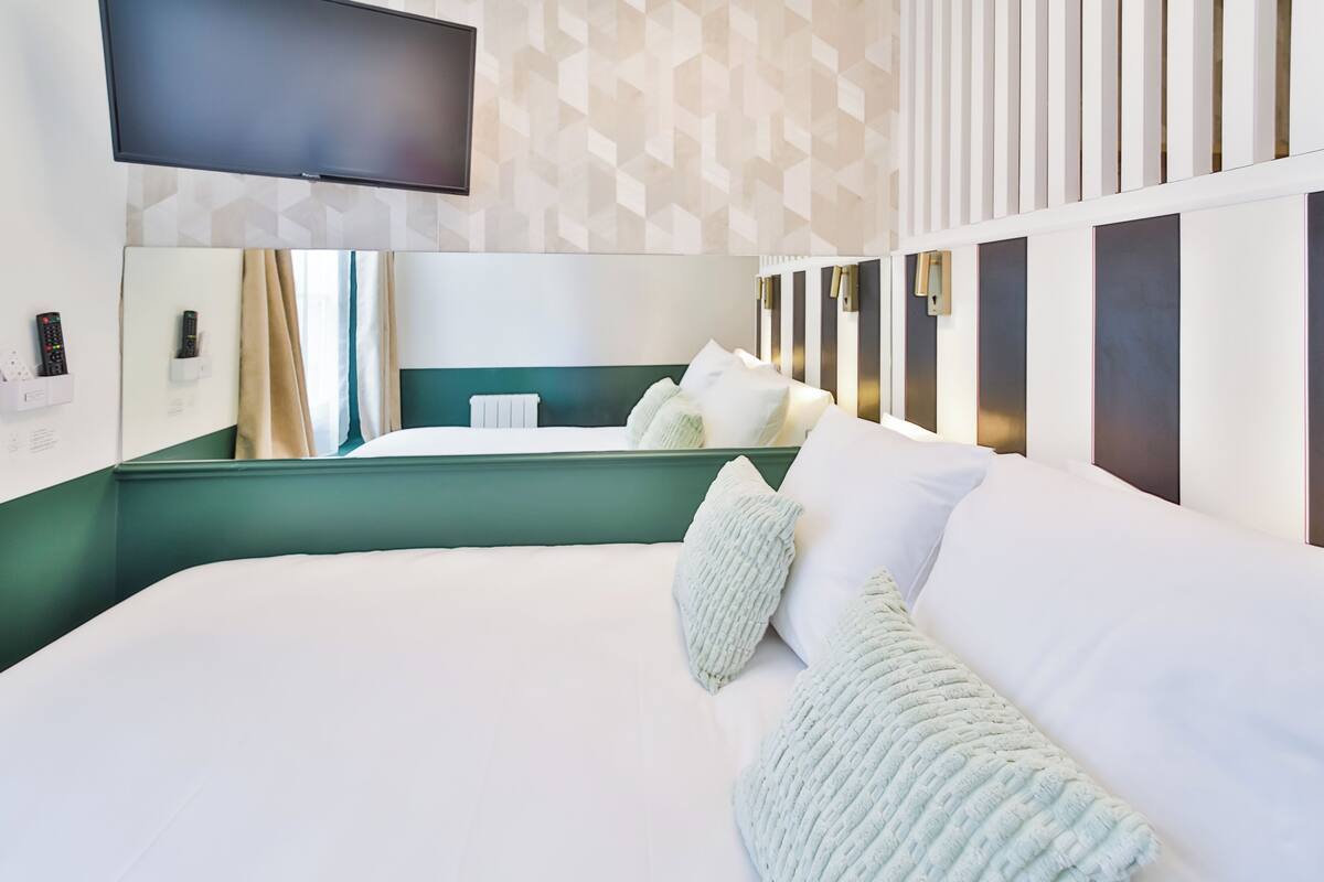 A modern hotel room with a large bed, a flat-screen TV mounted on the wall, and a geometric patterned wallpaper.