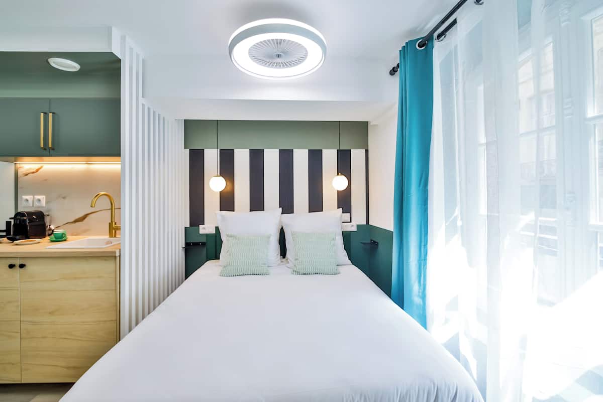 A modern hotel room with a bed, bedside lamps, a nightstand, a window with curtains, and a ceiling light.